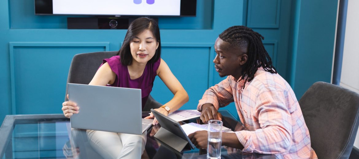 Asian woman and African American man looking at laptop screen together in a modern business office. She has black hair, he wears a checkered shirt, both young and focused, unaltered.
